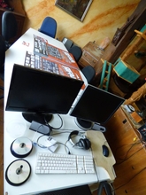 Auf einem Tisch stehen Monitore mit Tastatur davor. Im Hintergrund liegen Festivalplakate.